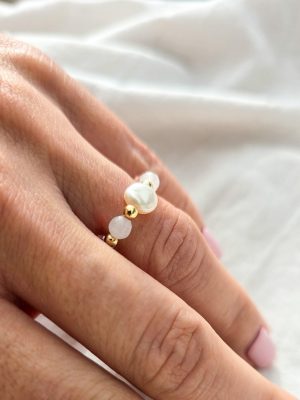 Ein Stretch-Ring an dem Ringfinger mit Glasperlen, Süßwasser-Zuchtperlen, Jade und 18K vergoldeten Elementen, fotografiert auf hellem Untergrund